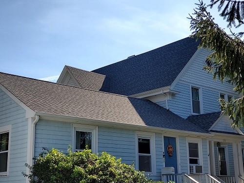 A blue Cape Cod style house with a gray shingle roof.