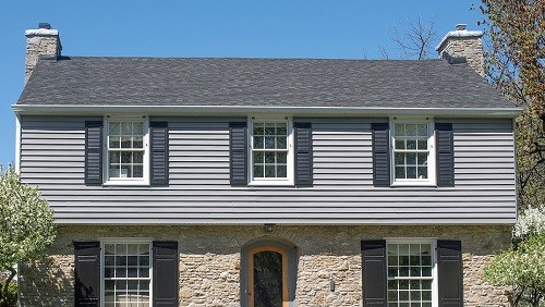 Two story home with gray siding and tan stone in spring.