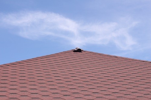 Roofing made of soft bituminous tiles of red color on the roof of a country house. Ventilation in the roof of a residential building.