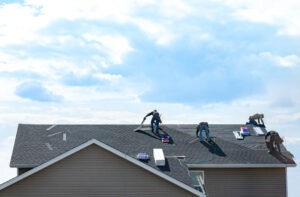Roofing professionals working on a grey roof of a suburban home