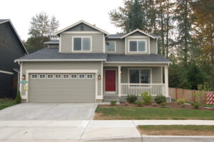 A grey suburban home with a garage door, grey siding and a red entry door