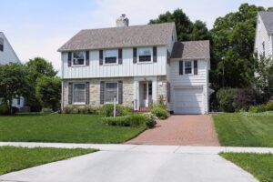 Two-story home with white board and batten siding on second level and stone siding on the first level