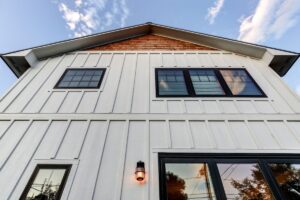 Looking up at a two-story home with white board-and-batten siding and black window and door frames