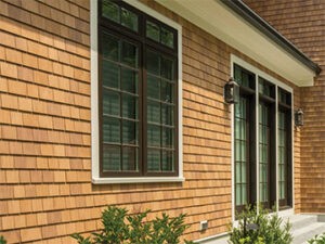 Home with light wooden cedar shake siding and window and patio door with brown grids